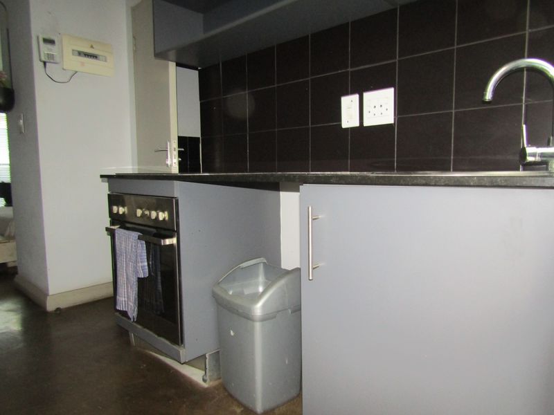 Compact kitchen featuring grey cabinetry, a built-in oven, black tiled splashback, and a stainless steel sink with a modern mixer tap.