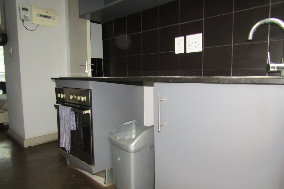 Compact kitchen featuring grey cabinetry, a built-in oven, black tiled splashback, and a stainless steel sink with a modern mixer tap.