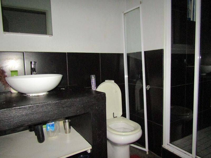 A compact bathroom featuring a vessel sink on a dark vanity, a toilet, and a shower enclosure with dark wall tiling.