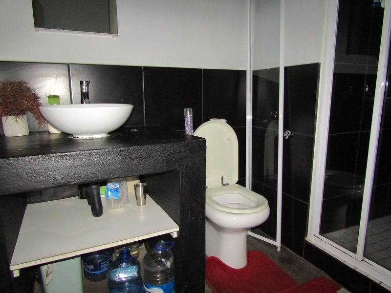 A bathroom featuring a vessel sink on a built-in vanity, a toilet, and a shower enclosure with black wall tiling.