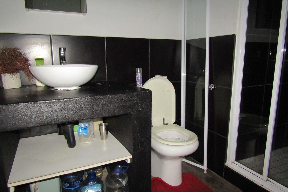 A bathroom featuring a vessel sink on a built-in vanity, a toilet, and a shower enclosure with black wall tiling.