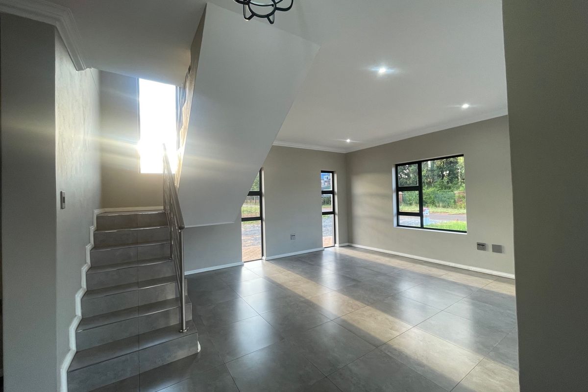 Spacious, modern open-plan living area featuring large format floor tiles, a contemporary staircase with stainless steel balustrade, and abundant natural light.