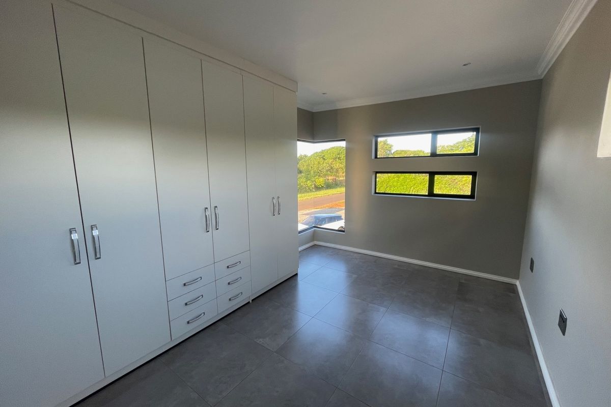 A modern, empty bedroom featuring extensive built-in cupboards, large corner and horizontal windows, and sleek grey floor tiles.