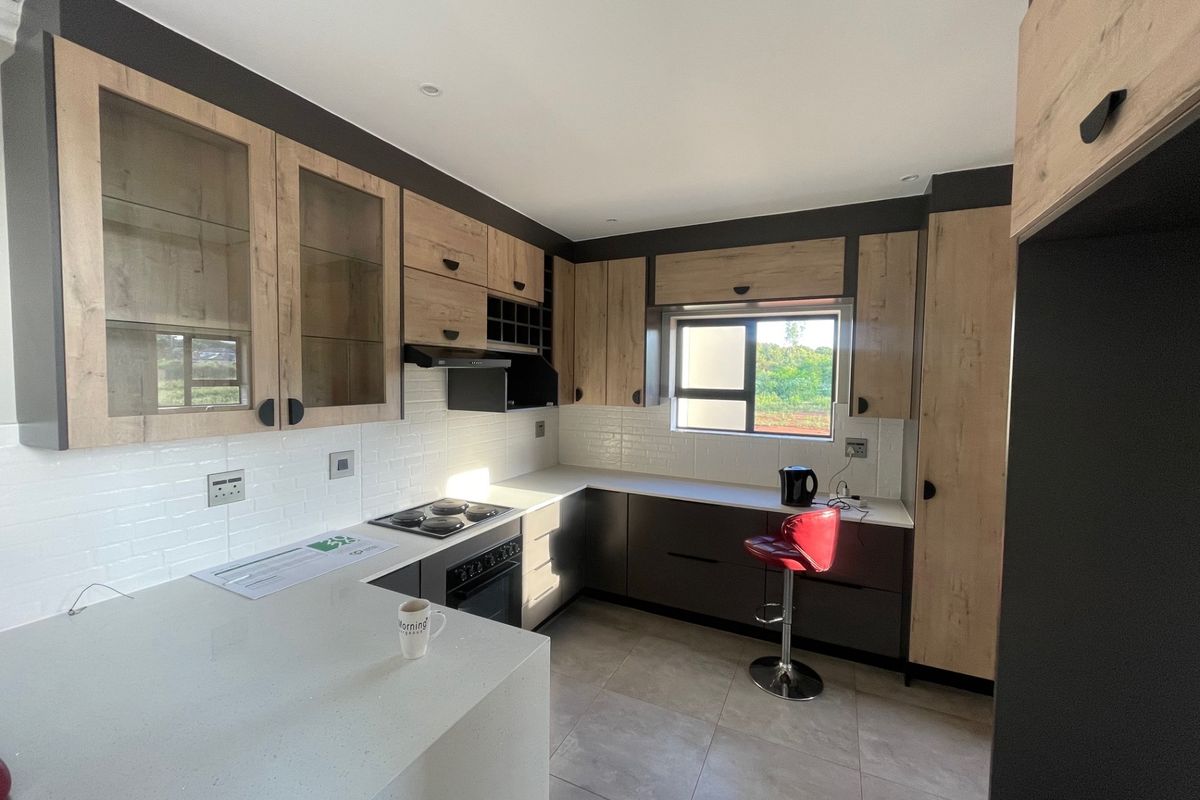 Modern kitchen featuring light wood-tone cabinetry, dark base units, quartz countertops, subway tile backsplash, and integrated appliances.