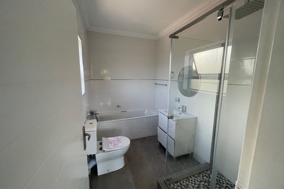 A functional bathroom featuring a bathtub, separate glass-enclosed shower, vanity unit, and toilet, finished with neutral wall and floor tiles.