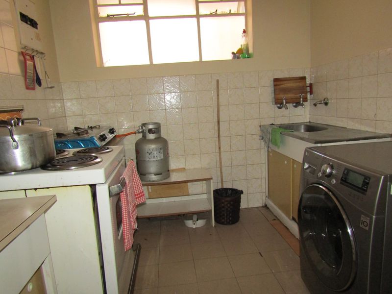 A functional kitchen area featuring tiled splashbacks, a stainless steel sink, and space for laundry appliances.