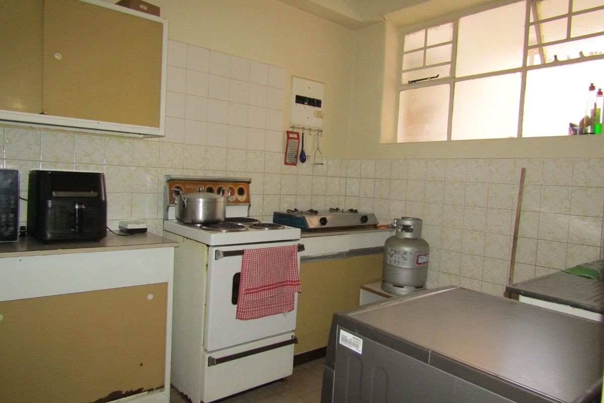 A dated kitchen featuring original cabinetry, tiled splashbacks, and a freestanding stove, offering significant potential for modernization and renovation.