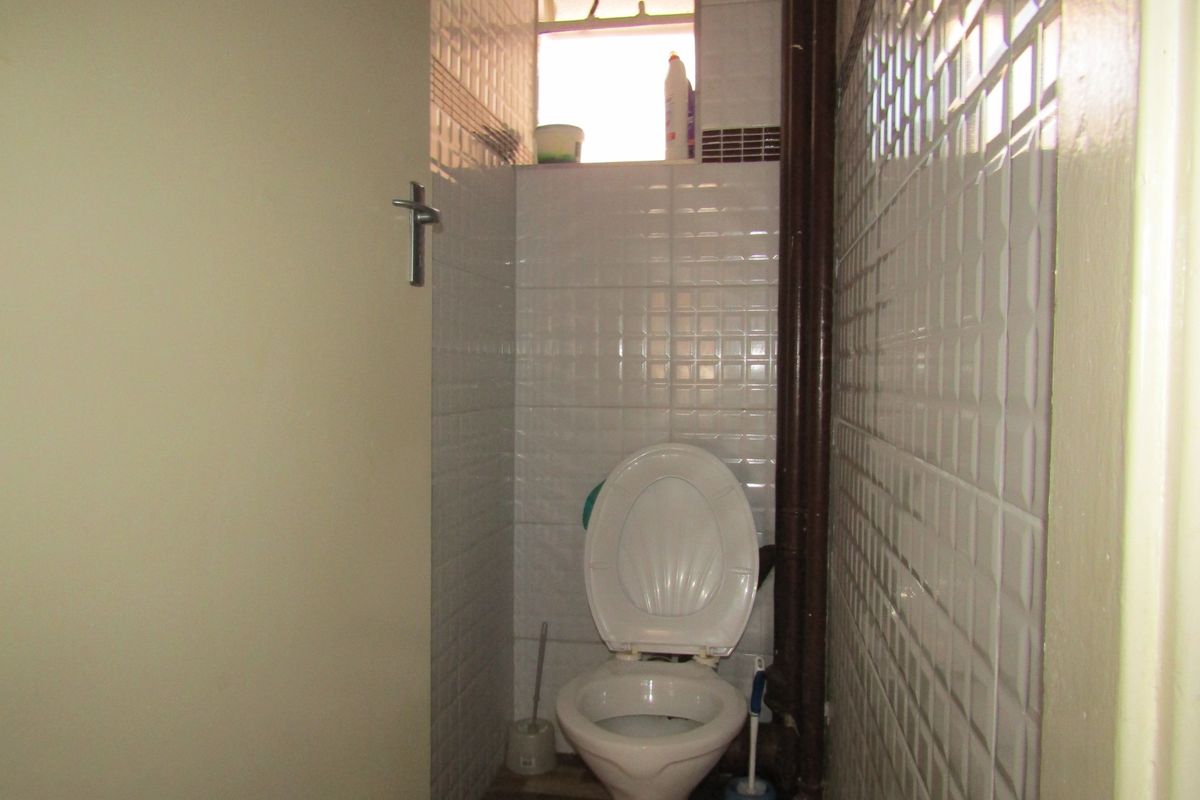 A small, dated bathroom featuring tiled walls and an exposed plumbing pipe.