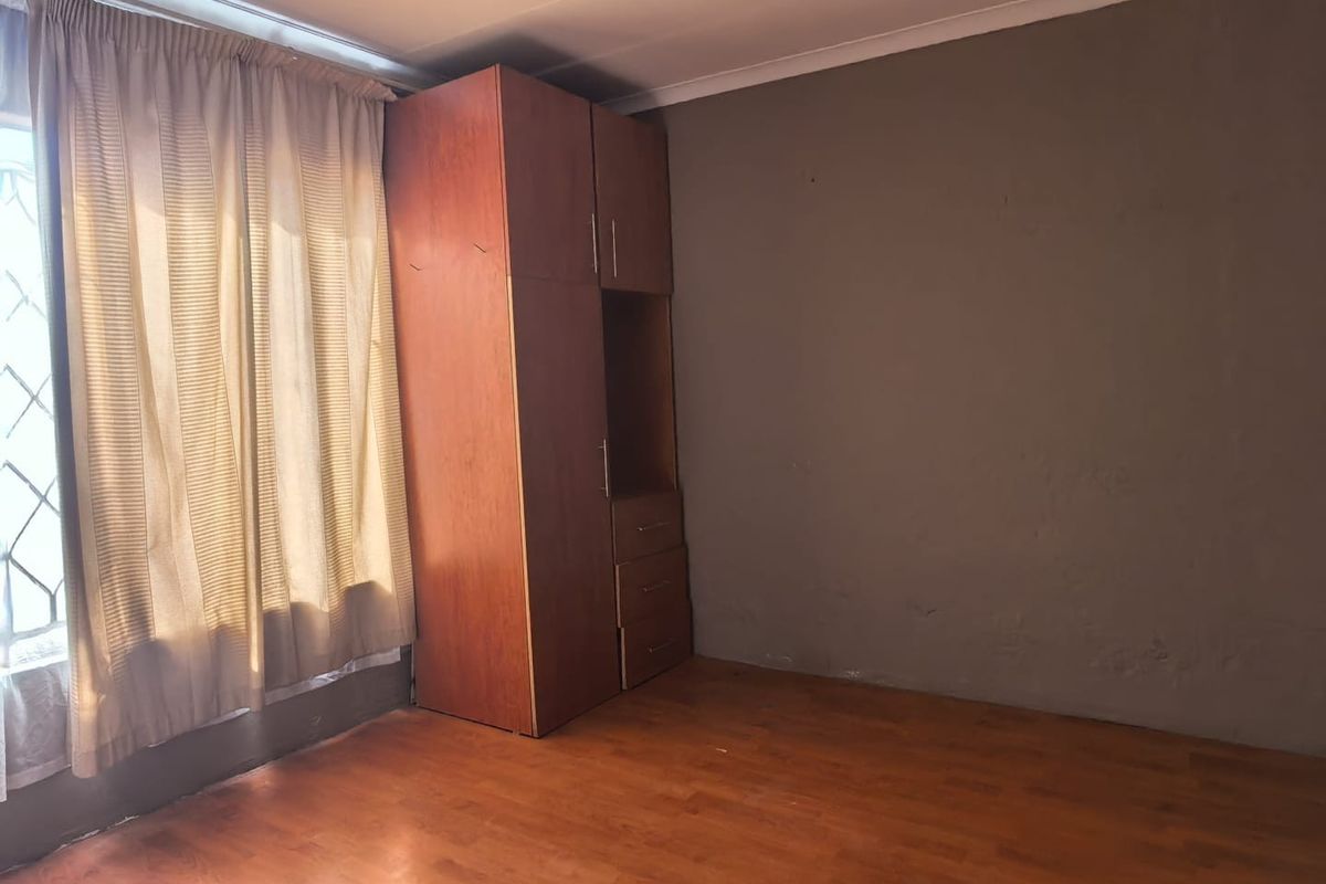 A bedroom featuring laminate flooring, a built-in wooden wardrobe, and neutral wall finishes, offering a blank canvas for personalization.