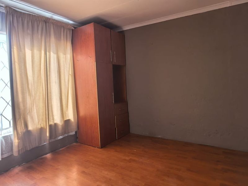 A bedroom featuring laminate flooring, a built-in wooden wardrobe, and neutral wall finishes, offering a blank canvas for personalization.