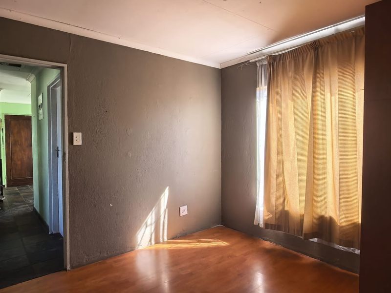 An empty bedroom featuring laminate flooring, neutral wall paint, and a window with an installed curtain rail.