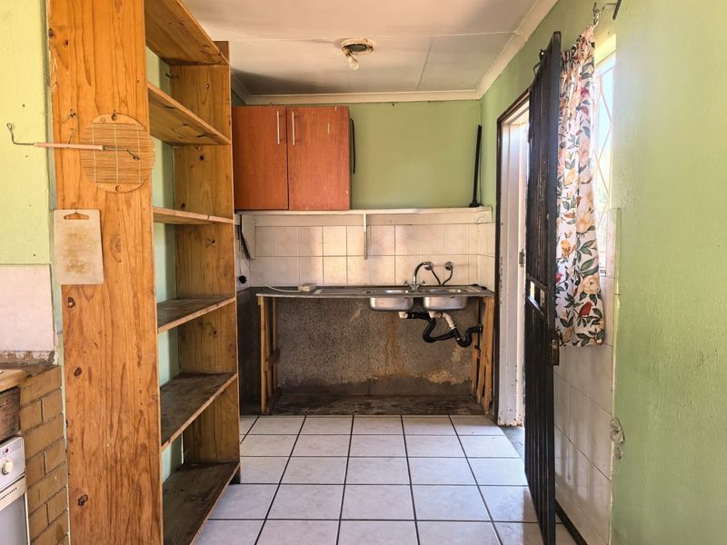 A functional scullery or utility area featuring a double sink, tiled splashback, and direct access to the exterior via a security gate.