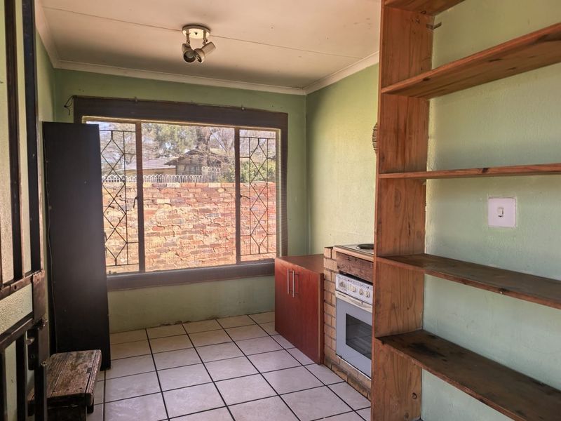 A functional kitchen space featuring built-in oven and hob, tiled flooring, and security bars on the window, offering potential for modernization.