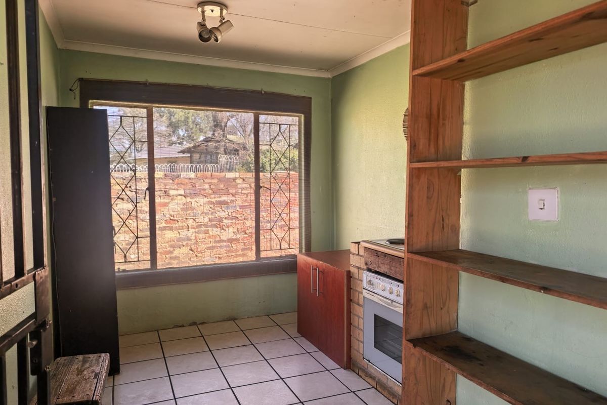 A functional kitchen space featuring built-in oven and hob, tiled flooring, and security bars on the window, offering potential for modernization.