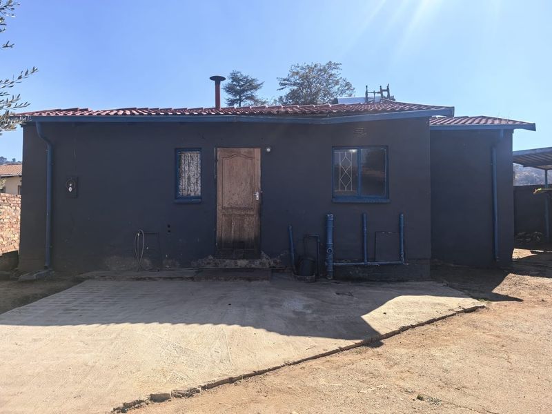 Rear exterior view of the house featuring a concrete patio, dark painted facade, and visible external plumbing infrastructure.