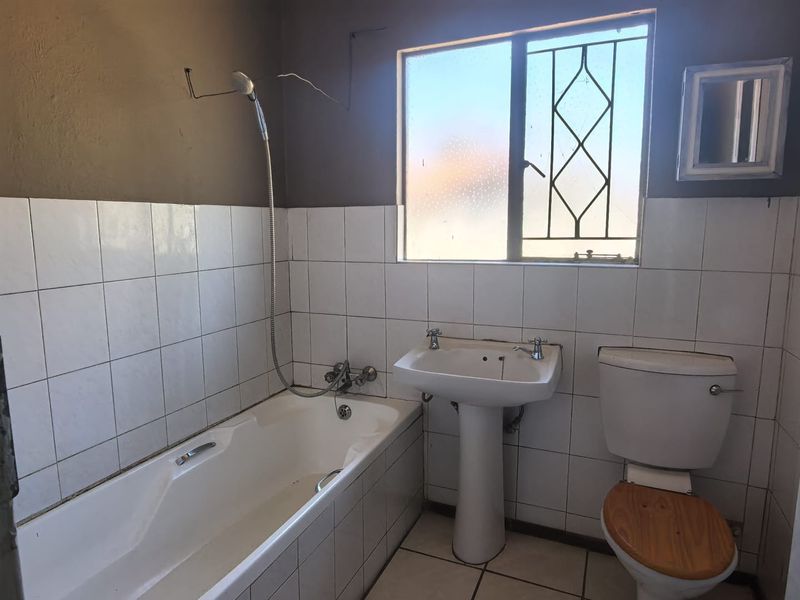A functional bathroom featuring a bathtub, pedestal basin, and toilet, with tiled finishes and security bars on the window.