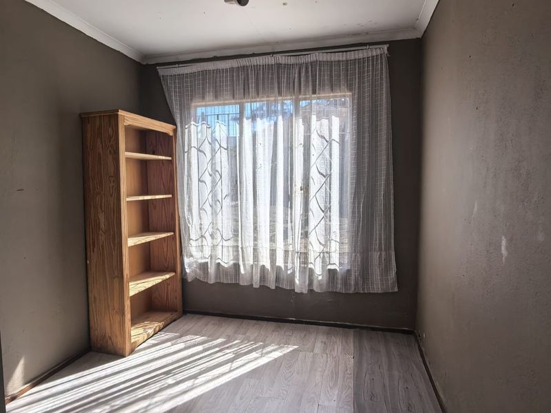 A simple bedroom featuring laminate flooring and security bars on the window, offering a blank canvas for renovation or restyling.