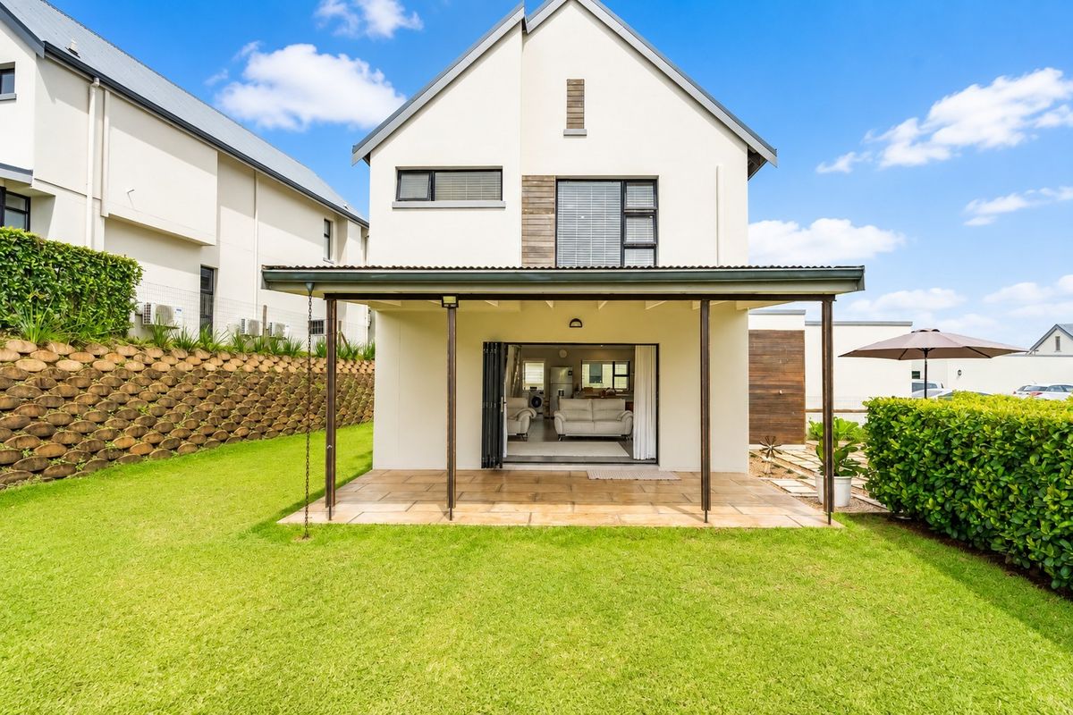Rear view of a two-story house featuring a covered patio with tiled flooring, bi-fold doors, and a well-maintained garden with a retaining wall.