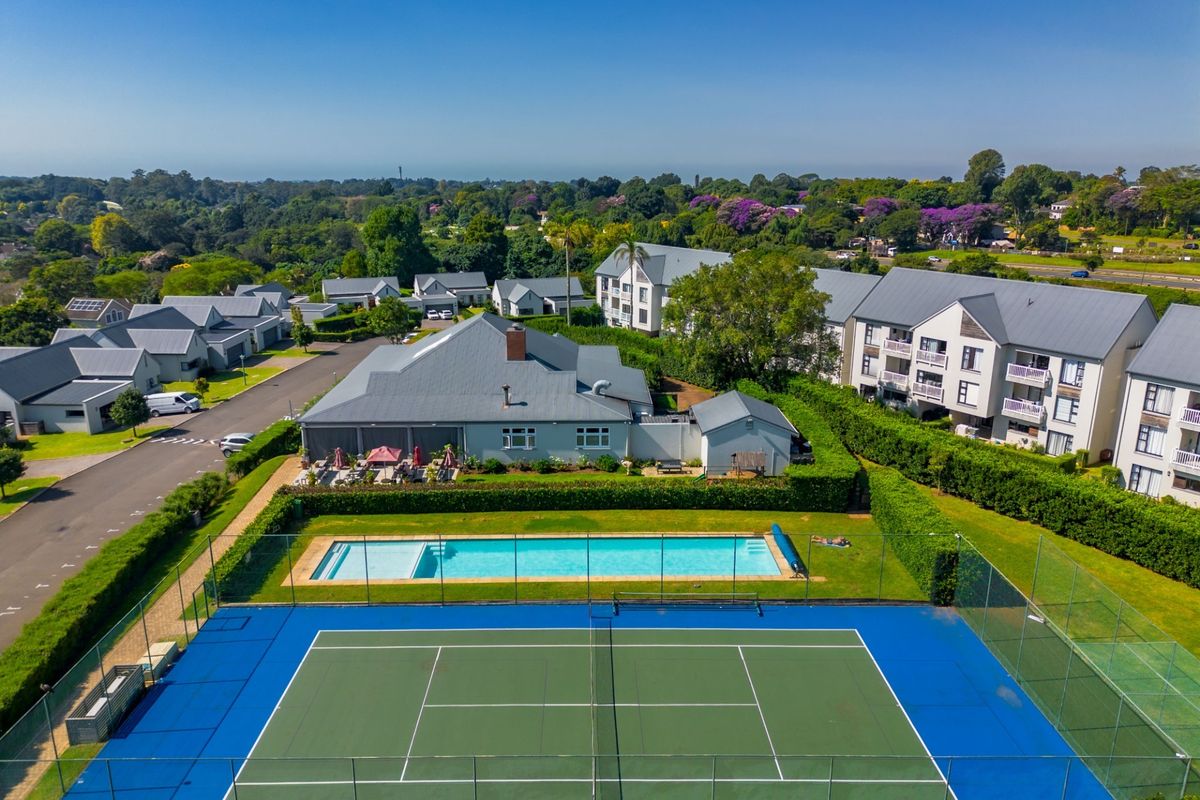 Aerial view of a residential property featuring a private swimming pool, tennis court, and well-maintained landscaped grounds within a secure estate setting.