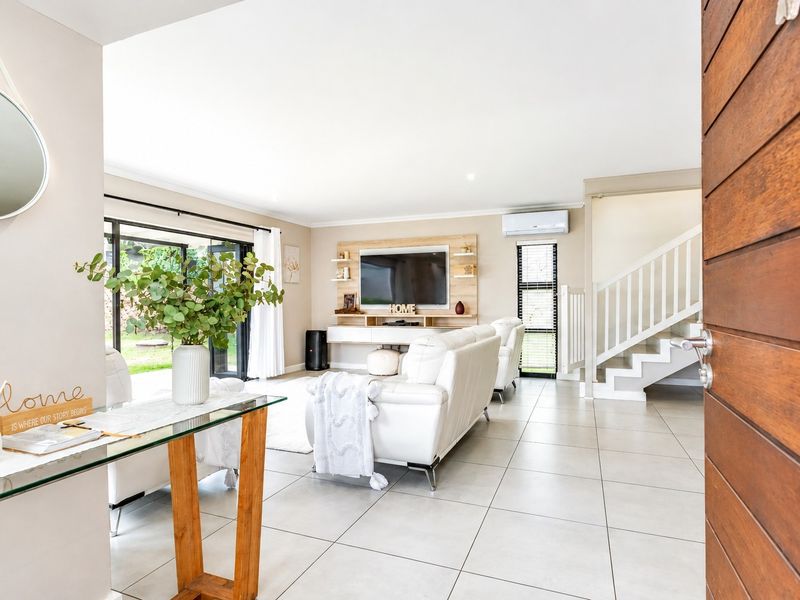 Bright and modern open-plan living area featuring tiled floors, a built-in media unit, split-system air conditioning, and direct access to the outdoor space.