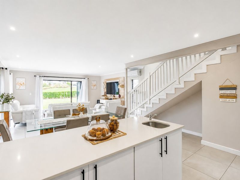 Bright open-plan living area featuring a modern kitchen island, tiled flooring, and a staircase, with seamless flow to the outdoor patio area.