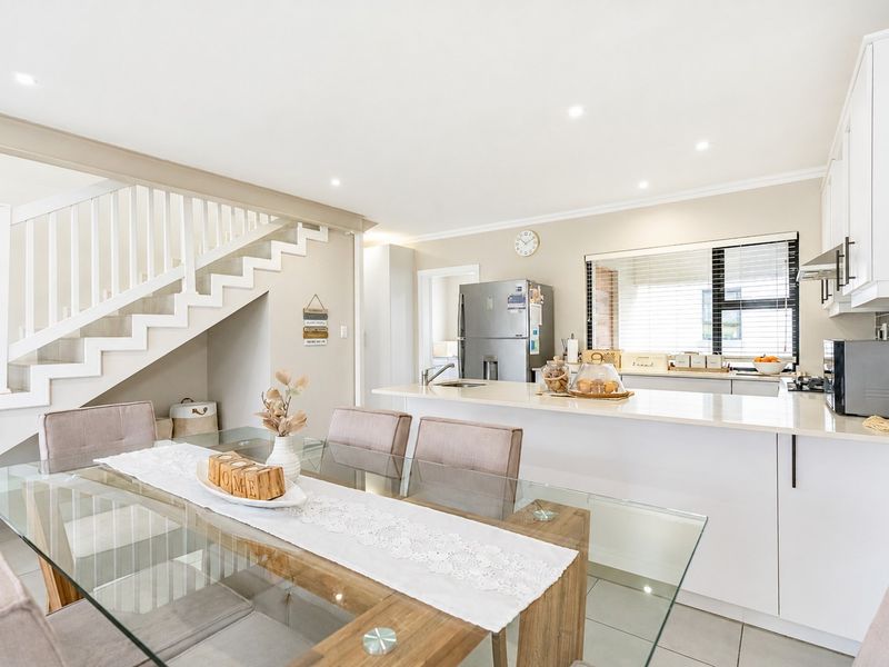 Bright open-plan kitchen and dining area featuring a central island, modern cabinetry, and a staircase with a white balustrade.