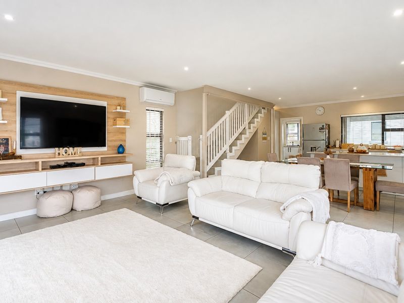 Spacious open-plan living and dining area featuring tiled floors, a modern built-in media unit, and a staircase leading to the upper level.