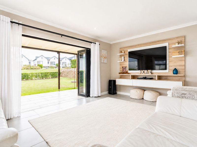 Modern living room featuring a built-in media wall, tiled floors, and large bi-fold doors opening onto a covered patio and garden.