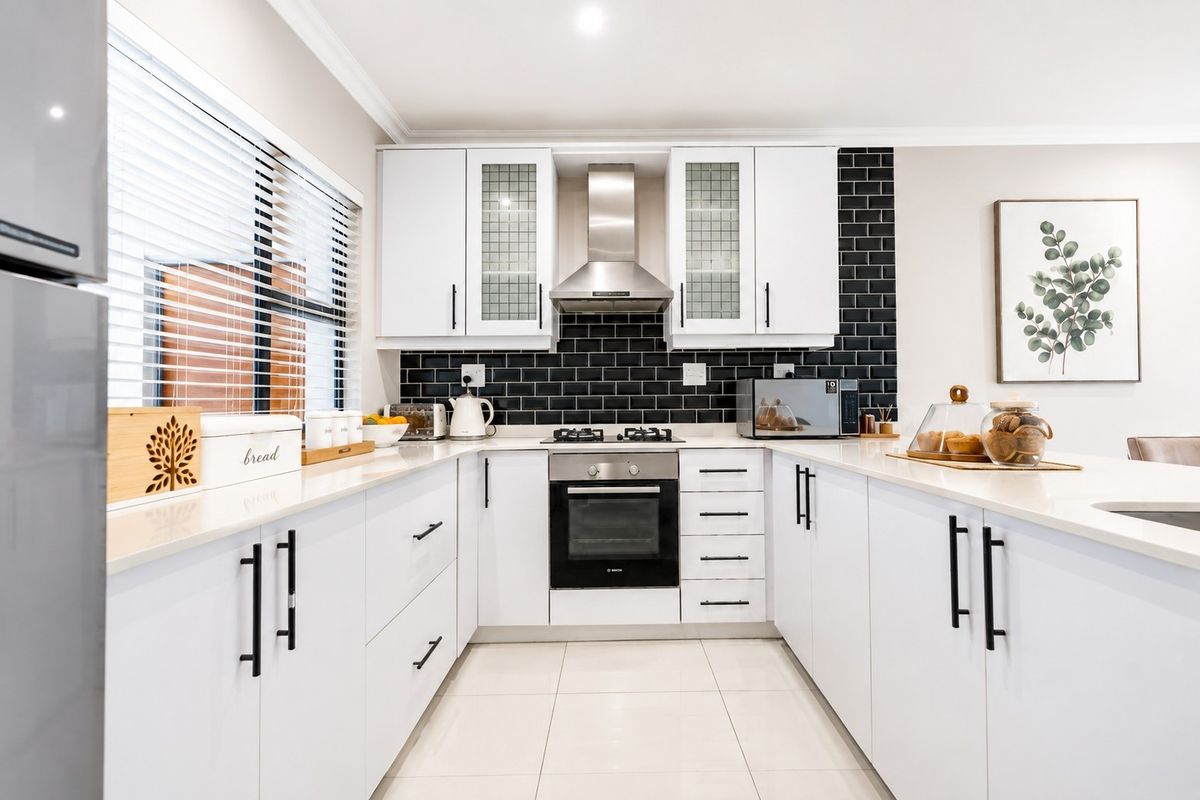 Modern kitchen featuring white cabinetry, quartz countertops, a striking black subway tile backsplash, and integrated stainless steel appliances.