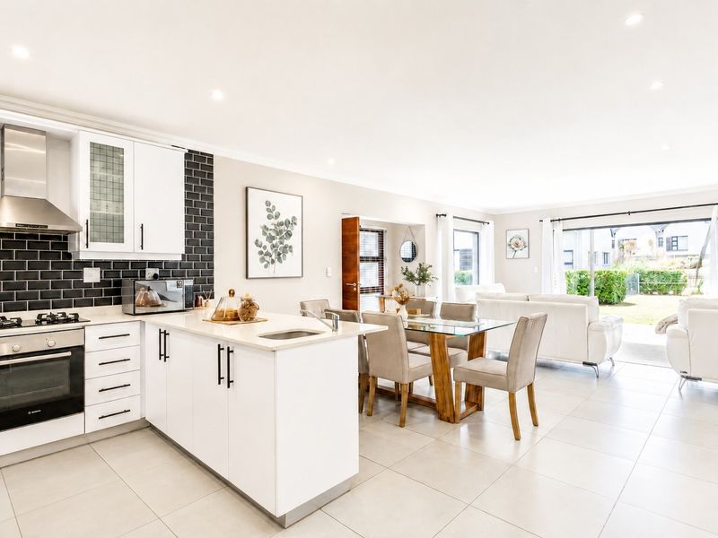 Modern open-plan kitchen and dining area featuring a central island, sleek white cabinetry, subway tile backsplash, and seamless flow to the outdoor patio.