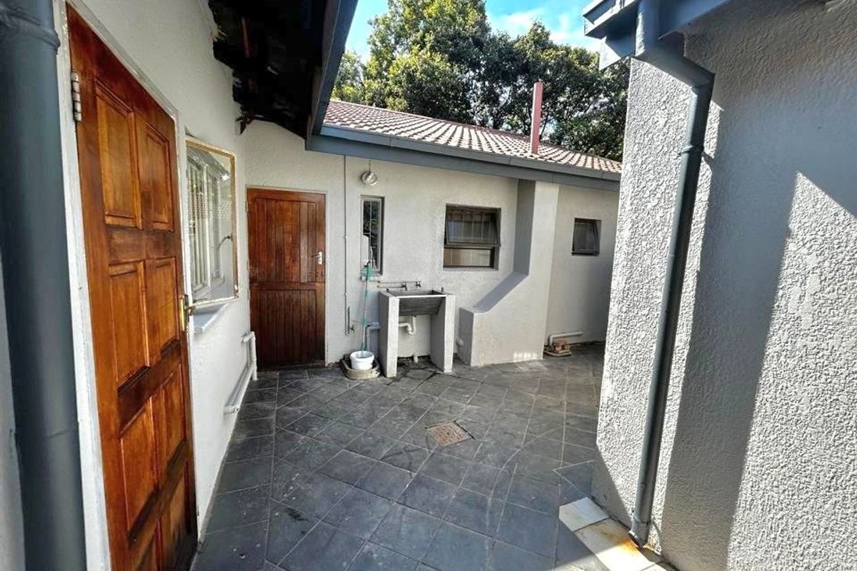 A paved rear courtyard area featuring an external utility sink, timber access doors, and functional drainage infrastructure.