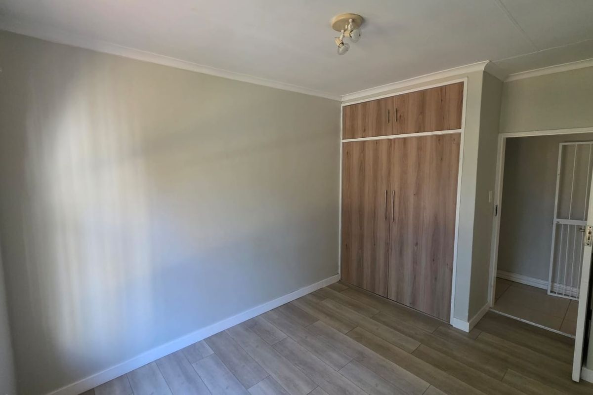 A bright, empty bedroom featuring modern wood-look laminate flooring and built-in cupboards with overhead storage.