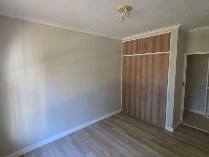 A bright, empty bedroom featuring modern wood-look laminate flooring and built-in cupboards with overhead storage.