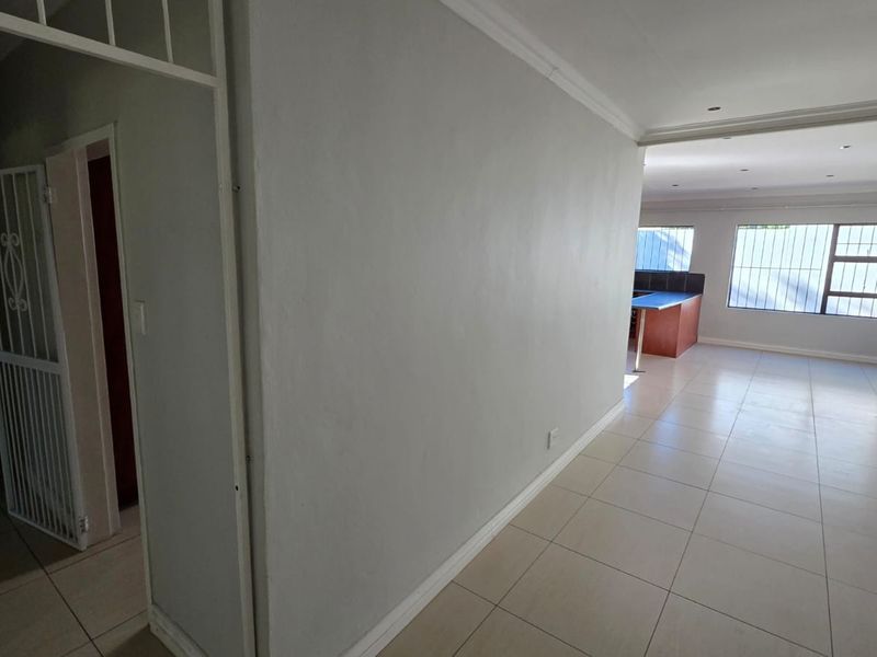 Spacious open-plan living area featuring neutral tiled flooring, recessed lighting, and secure window bars, offering a versatile layout for modern living.