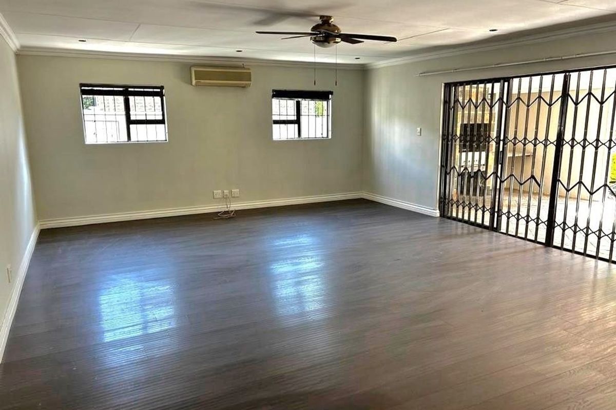 Spacious, empty living area featuring laminate flooring, a ceiling fan, split-system air conditioning, and sliding glass doors with security gates leading outdoors.