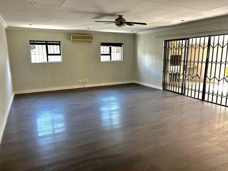 Spacious, empty living area featuring laminate flooring, a ceiling fan, split-system air conditioning, and sliding glass doors with security gates leading outdoors.