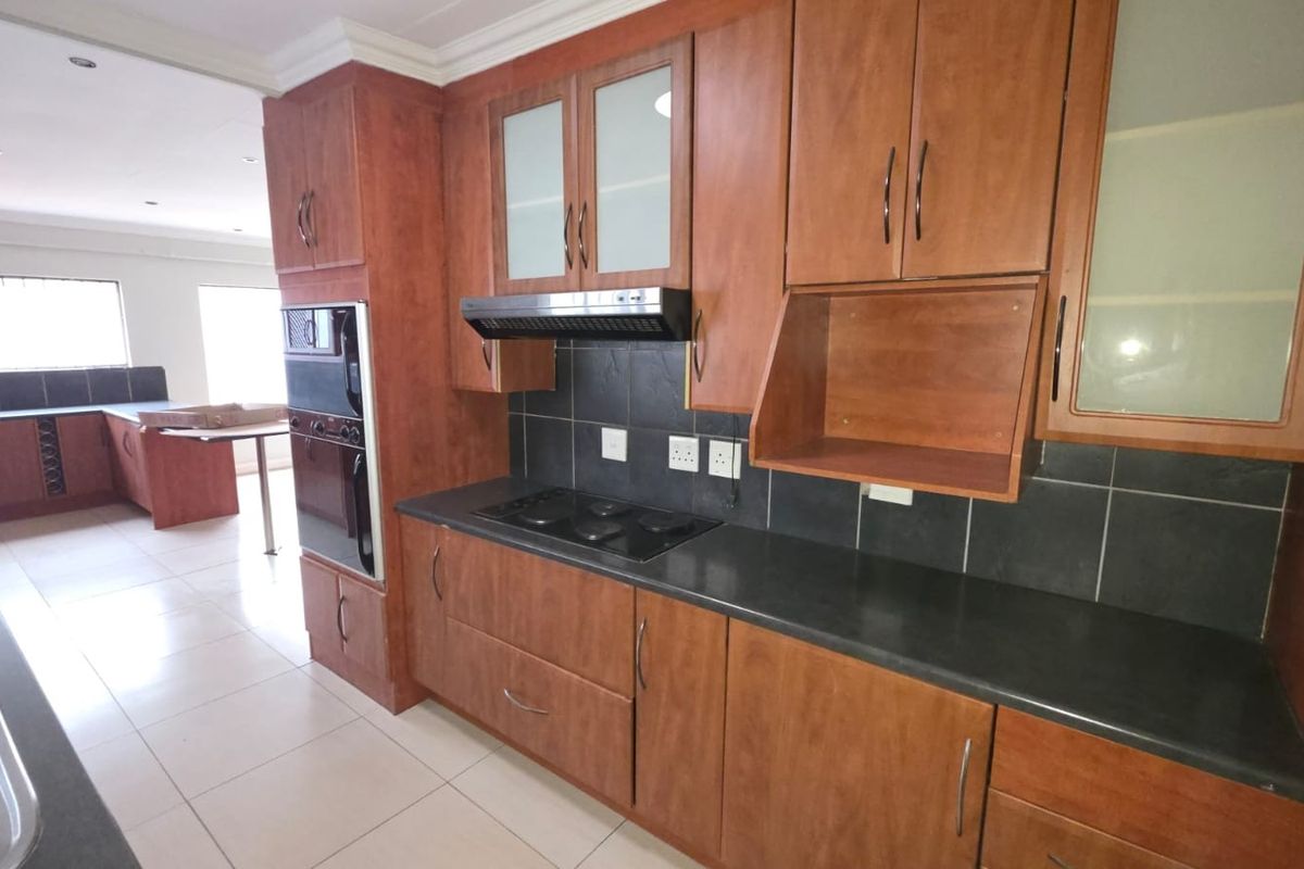 A spacious kitchen featuring wood-finish cabinetry, dark countertops, a built-in oven, electric hob, and tiled flooring, offering a functional layout for culinary activities.