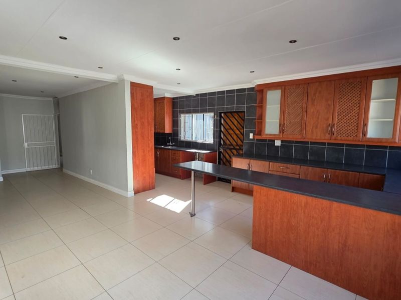 Spacious open-plan kitchen and living area featuring wooden cabinetry, a breakfast bar, tiled flooring, and recessed lighting throughout.