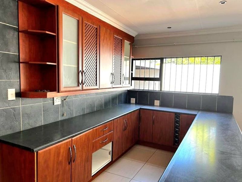 A clean, functional kitchen featuring warm-toned wooden cabinetry, dark laminate countertops, and a tiled backsplash, offering ample storage and workspace.
