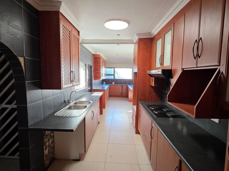 Spacious galley-style kitchen featuring extensive wooden cabinetry, dark countertops, integrated hob, and double sink, offering a functional layout with ample storage space.