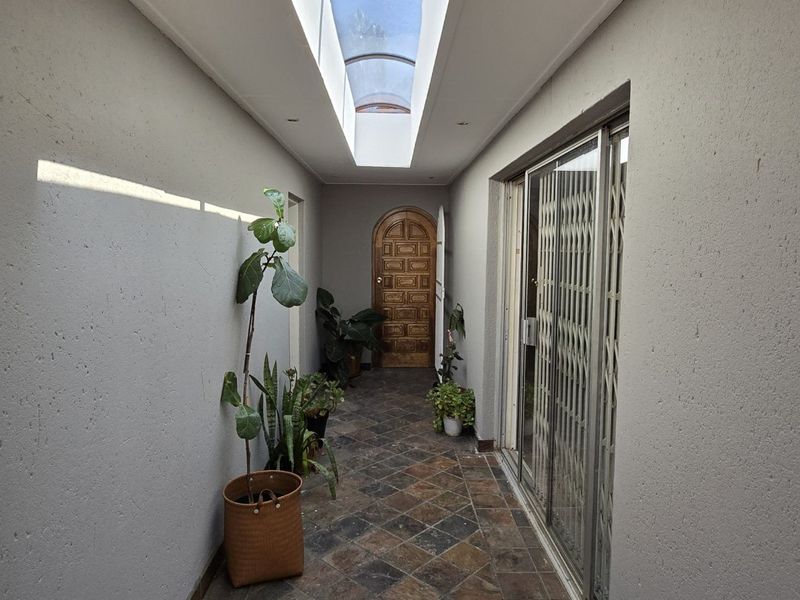 A bright hallway featuring tiled flooring, a central skylight, and access to adjacent rooms through a sliding glass door and a timber door.