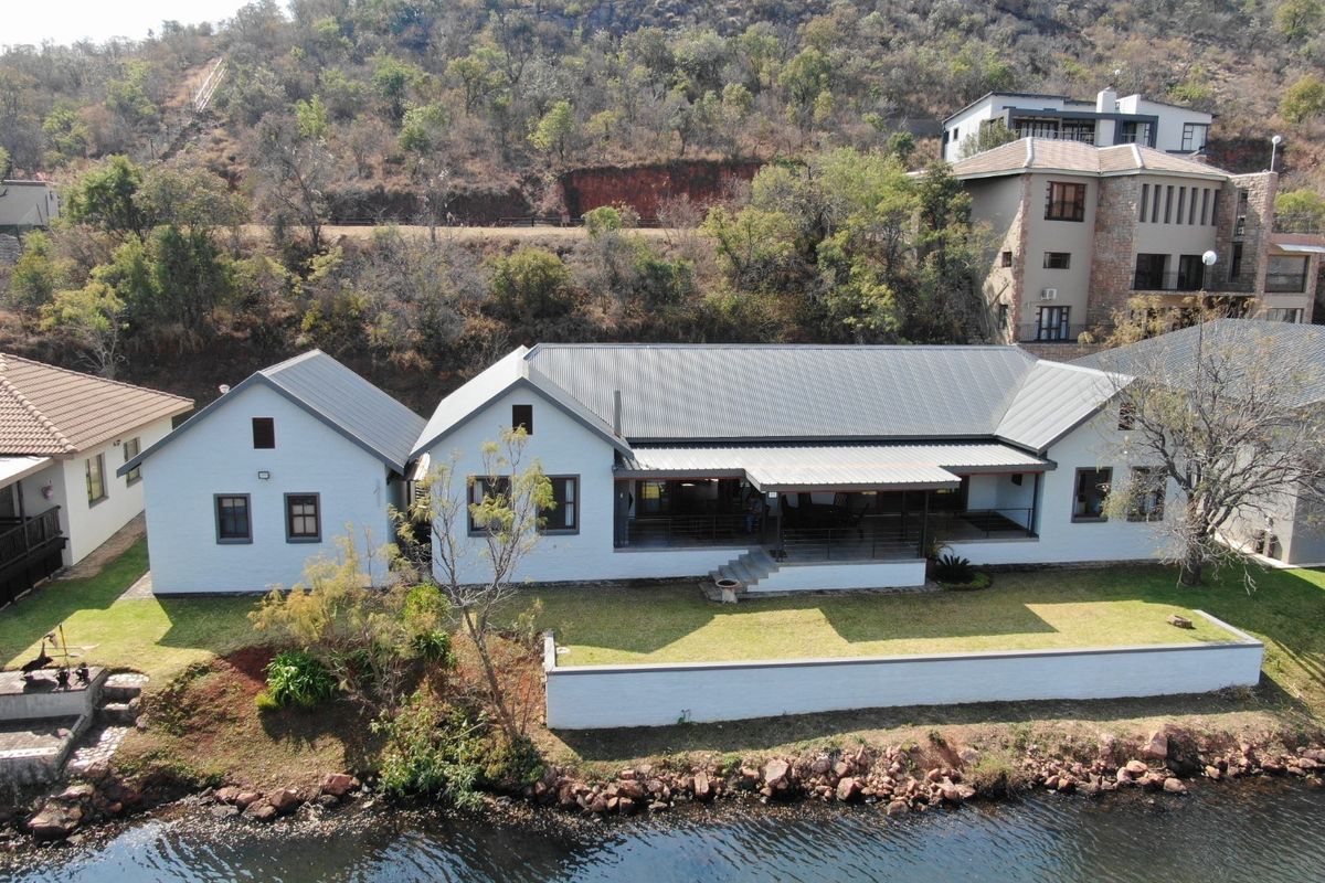 Aerial view of a well-maintained waterfront house featuring a metal roof, covered patio, and landscaped garden area.