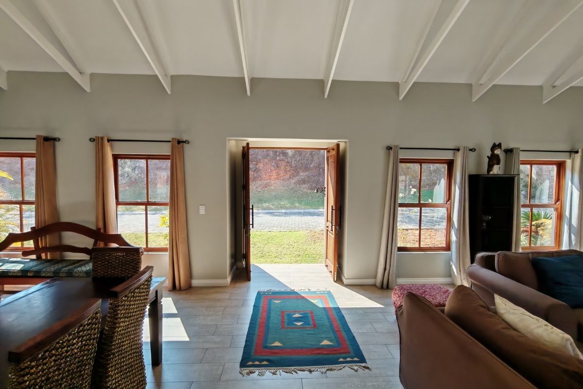Spacious living area featuring high vaulted ceilings with exposed beams, tiled flooring, and large timber-framed windows providing natural light and garden access.
