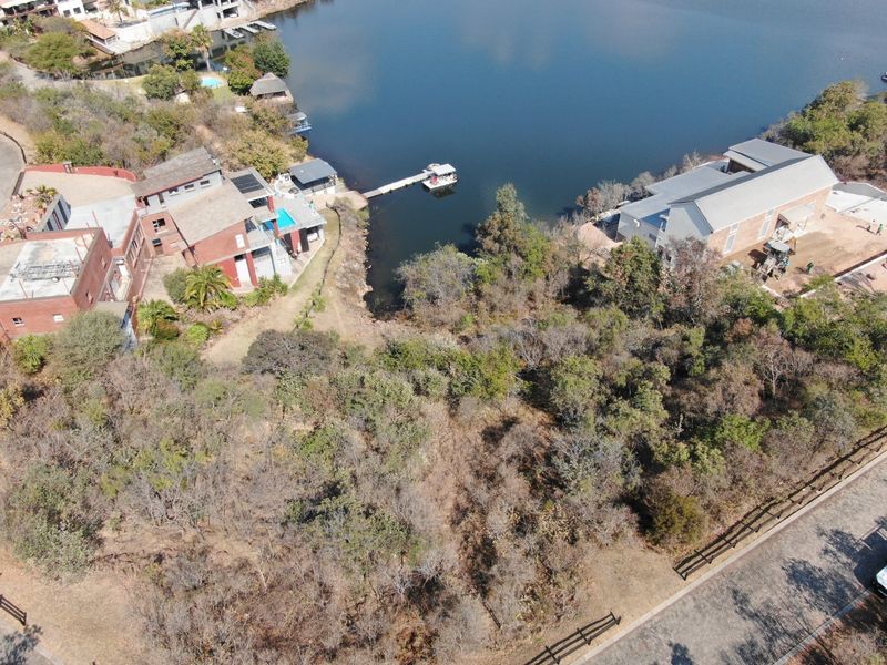 Aerial view of a vacant residential plot featuring direct waterfront access, a private jetty, and established vegetation in a scenic estate setting.