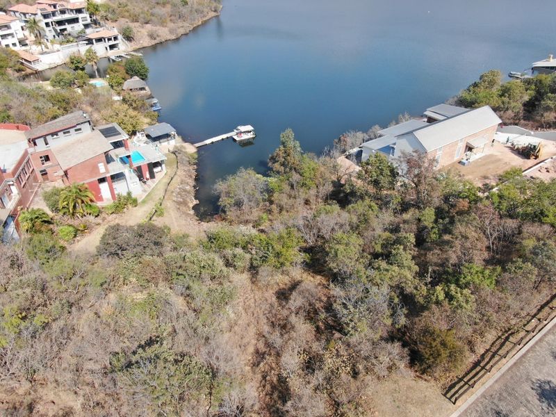 Aerial view of a vacant residential plot featuring natural vegetation and direct waterfront access within a developed estate setting.