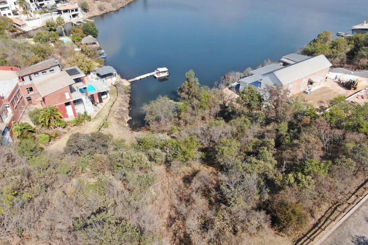 Aerial view of a vacant residential plot featuring natural vegetation and direct waterfront access within a developed estate setting.