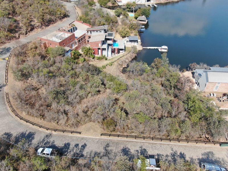 Aerial view of a residential property featuring a large vacant plot, waterfront access with a private dock, and proximity to a swimming pool.