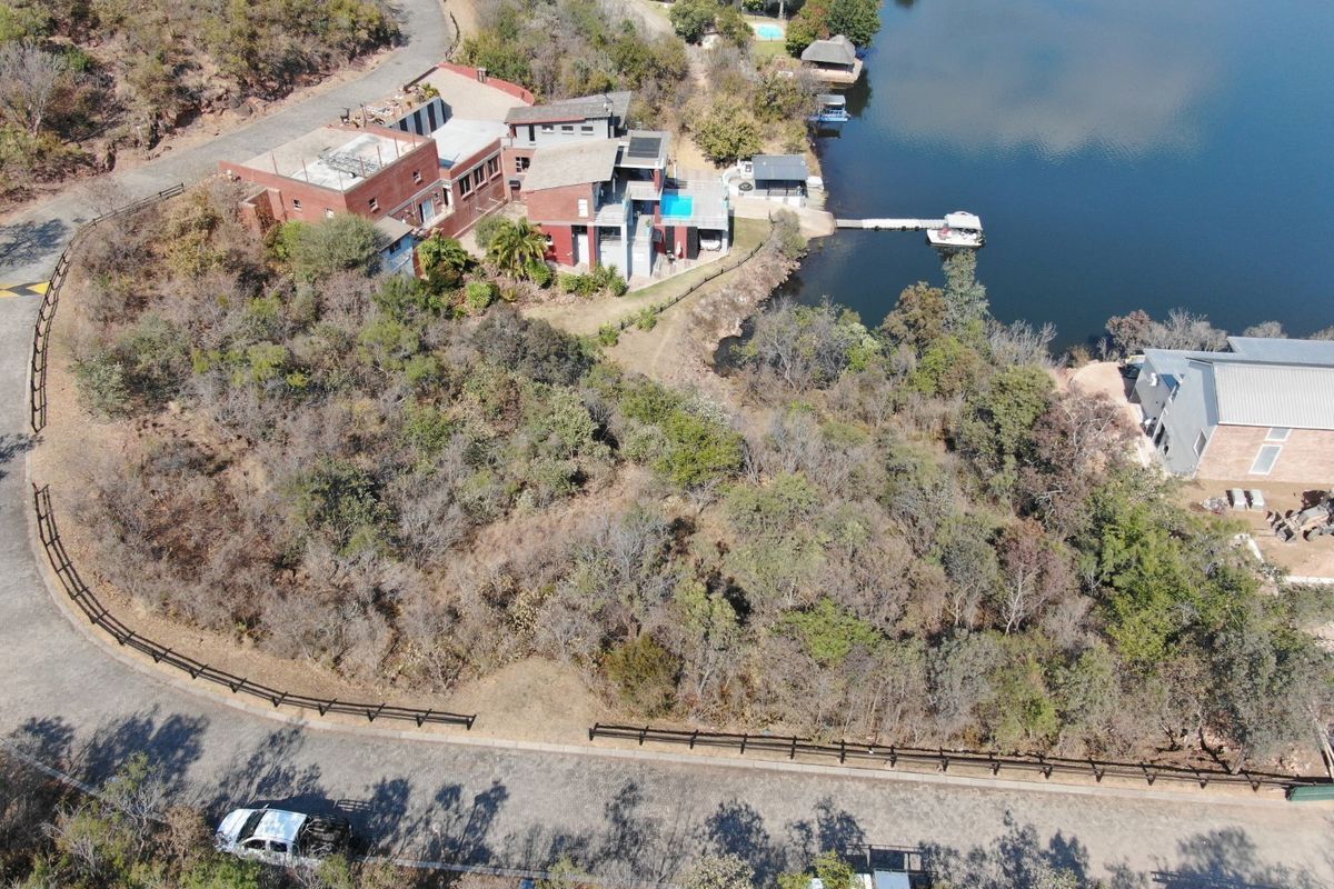 Aerial view of a residential property featuring a large vacant plot, waterfront access with a private dock, and proximity to a swimming pool.