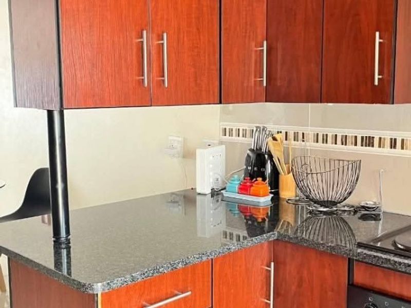 Compact kitchen featuring dark wood-look cabinetry, granite countertops, a built-in oven, and a decorative tiled backsplash.