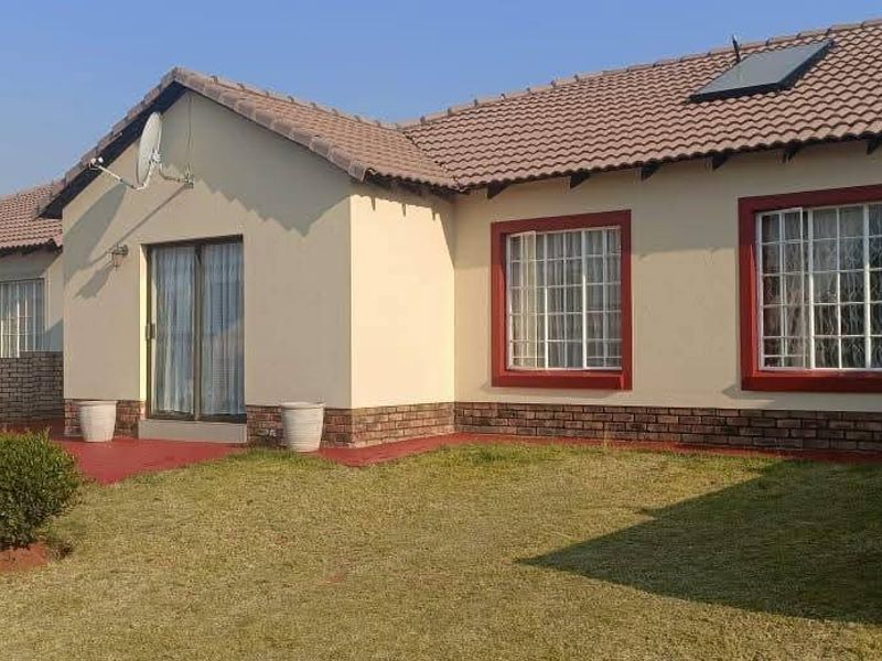 Rear view of the house featuring a tiled roof, brick boundary walls, a sliding glass door, and a small lawn area.